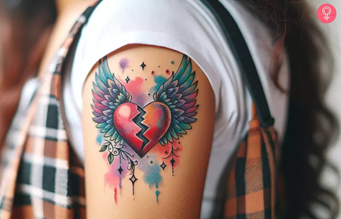 A vibrant broken heart with wings tattooed on the upper arm