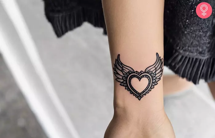 A woman sporting a small heart with wings tattoo on the wrist