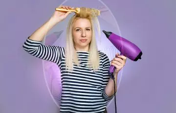 A woman using a hair dryer and a brush and looking at mirror