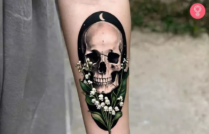 A woman with a lily of the valley and skull tattoo on her forearm