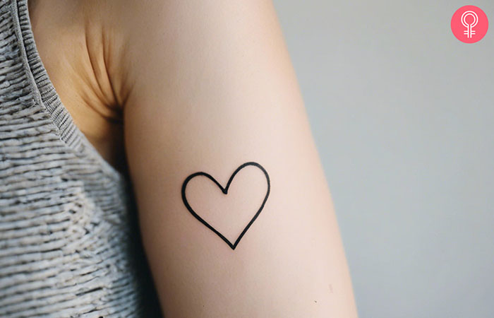 A woman with a minimalist heart tattoo on her upper arm
