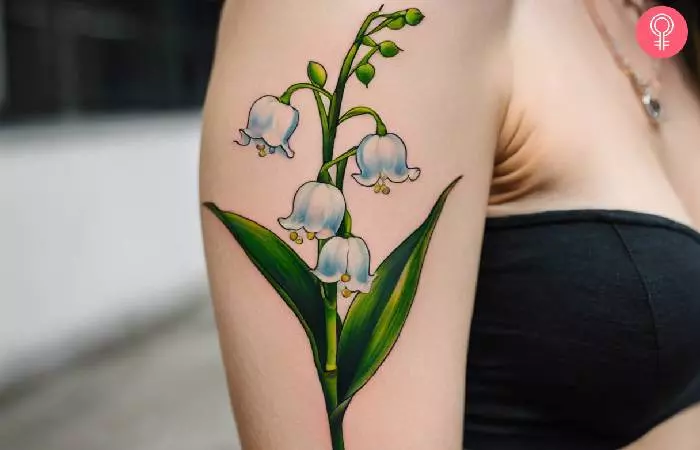 A woman with a realistic lily of the valley tattoo on the upper arm
