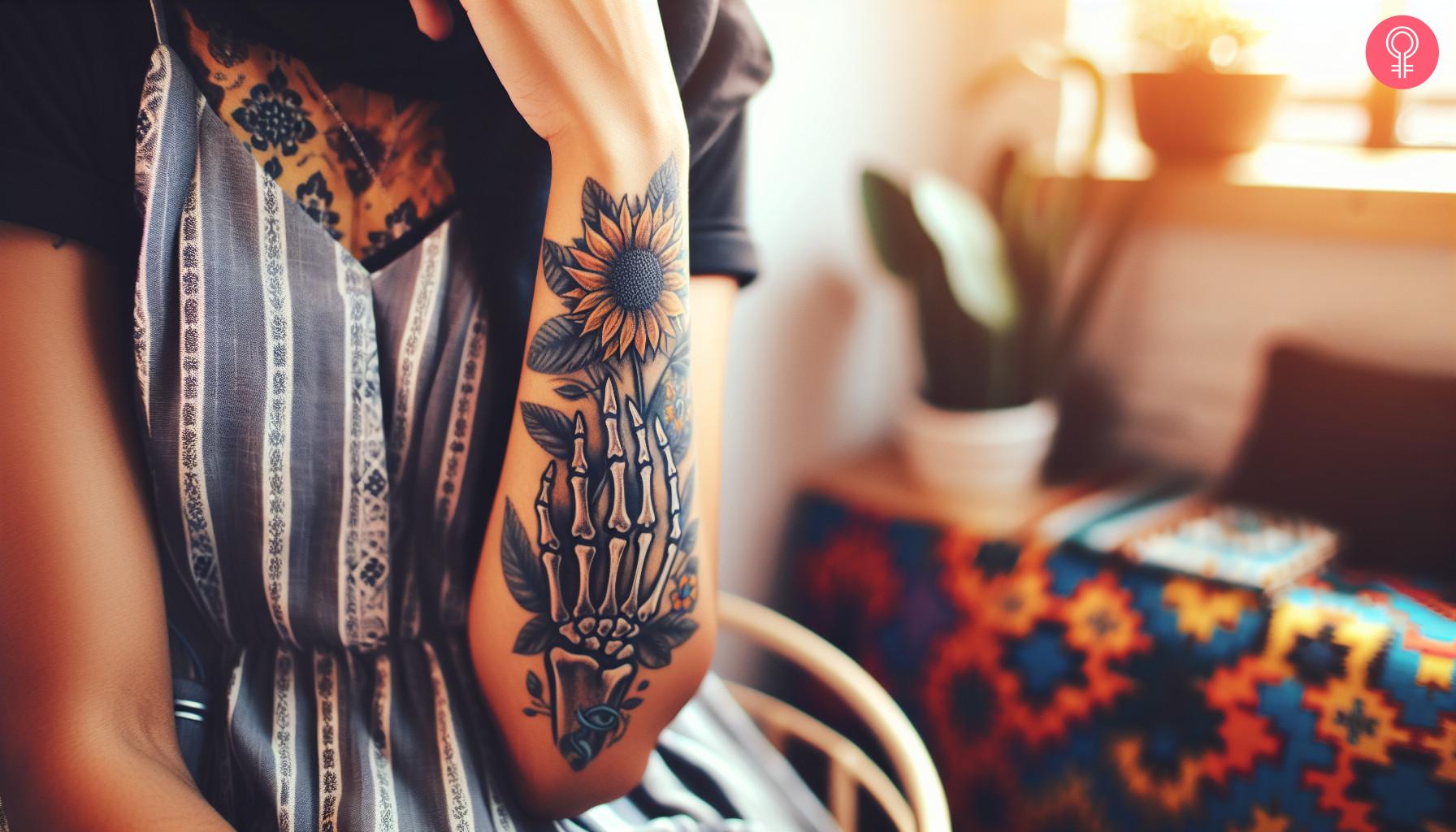 A woman with a skeleton hand holding a sunflower tattoo on her forearm