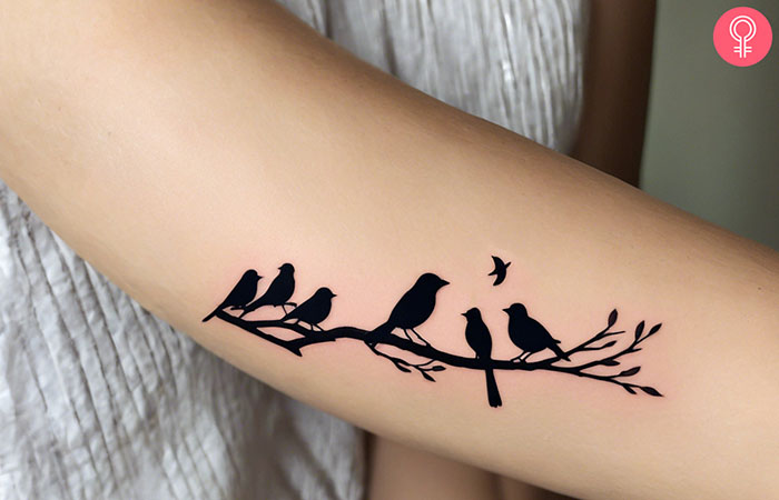A woman with a tattoo of birds on a branch on her forearm.