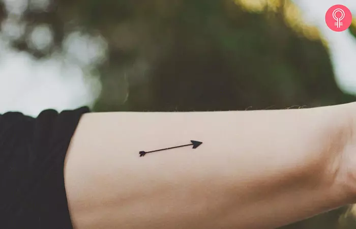 A woman with a tiny stick and poke bow and arrow tattoo on her upper arm