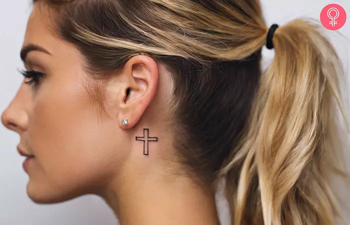 An outlined behind the ear cross tattoo on a woman