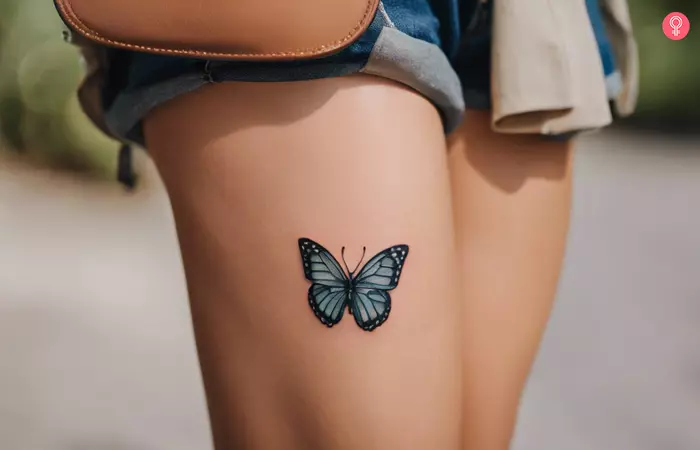 A simple blue butterfly tattoo on a woman’s thigh