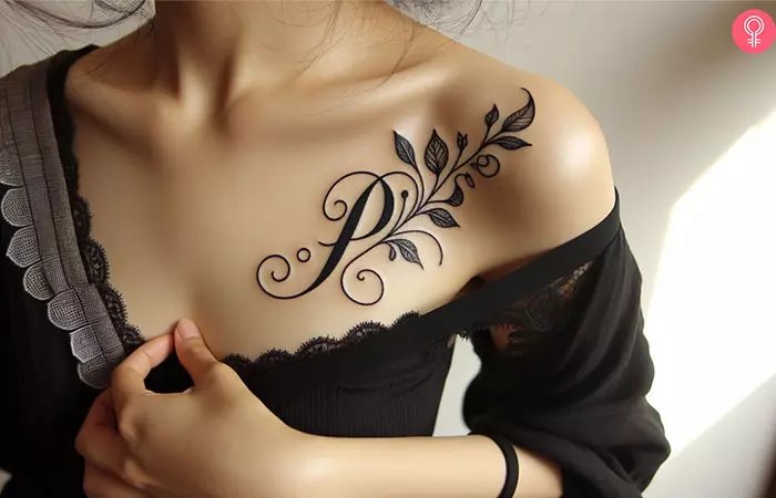 A cursive P tattoo along the collarbones and shoulder of a woman