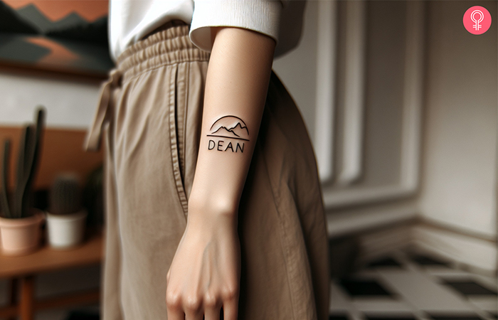 A forearm baby name tattoo with a mountain icon