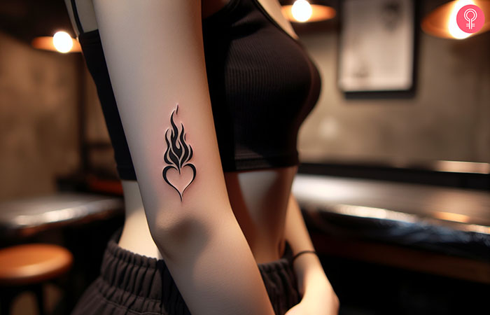 A heart on fire tattoo design on the arm of a woman