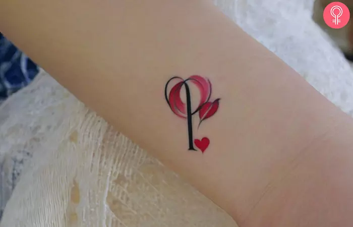 P tattoo with a red heart on the wrist of a woman