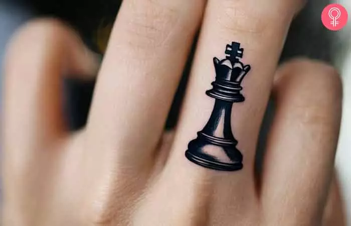 A hand with the king chess piece tattooed on the middle finger.