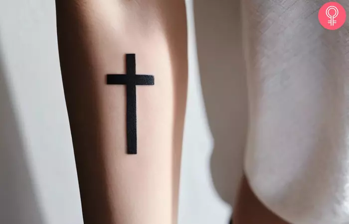 A woman wearing a small 3D cross tattoo on her arm