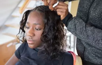 A young girl getting her hair in a sew-in hairstyle.