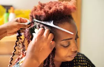 A woman getting her extensions done with a needle and thread by a hair stylist.