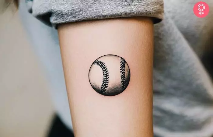 Woman with a small baseball tattoo on the forearm