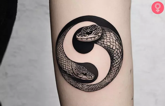 A yin yang snake tattoo on the arm of a woman