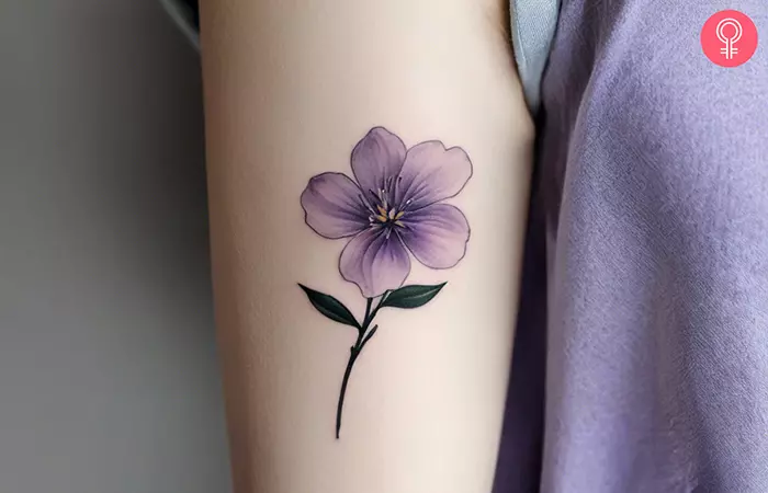 A minimalist lilac flower tattoo on the upper arm