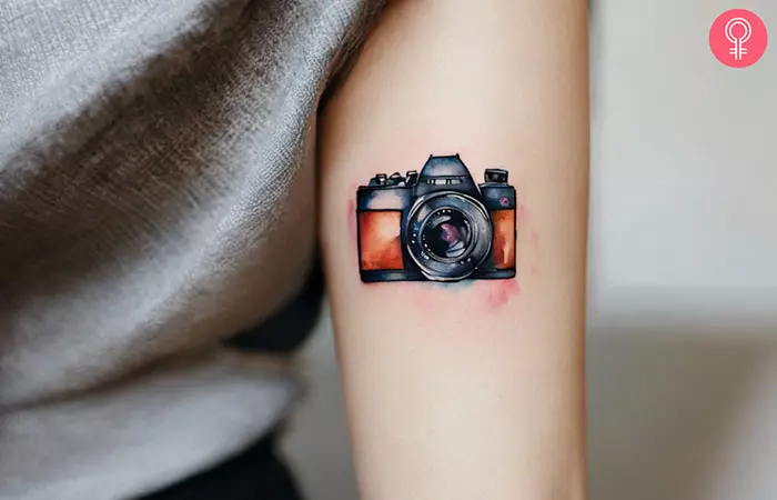 A small watercolor camera tattoo on the arm
