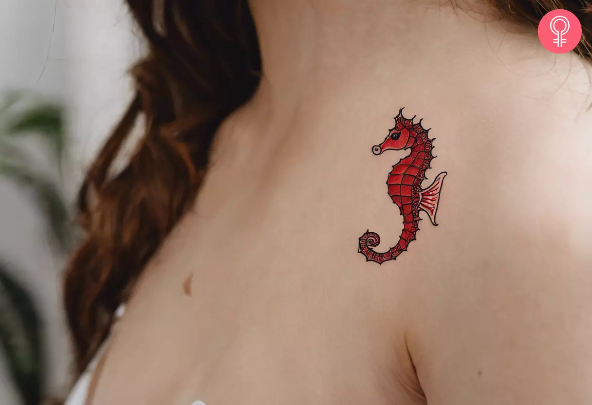 A woman flaunting a small red seahorse tattoo on the front side of her shoulder