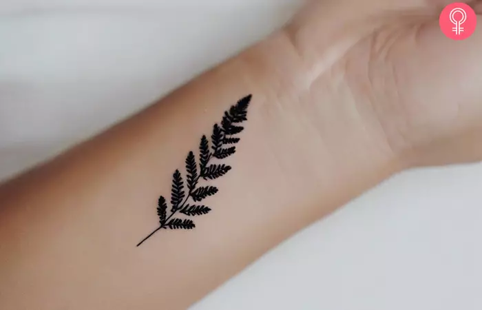 A small black fern tattoo on the wrist of a woman