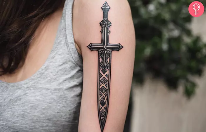 A woman with a black traditional dagger tattoo on her upper arm