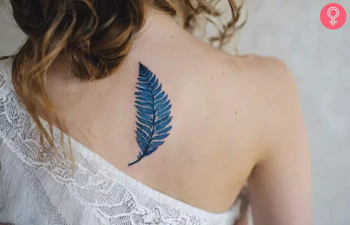 A small blue fern tattoo on the back of a woman