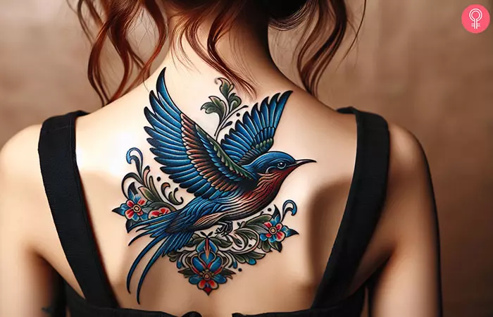 A tattoo of a flying bluebird on the upper back of a woman