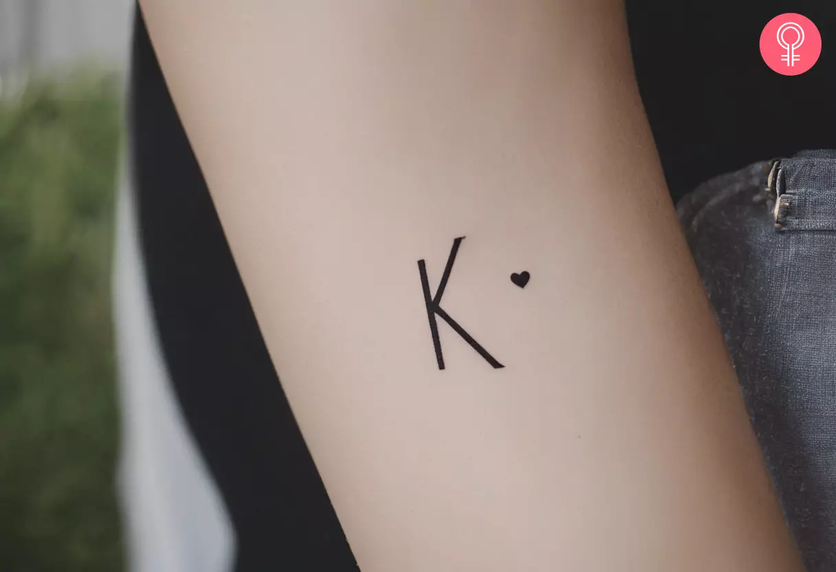 A letter K tattoo with a red heart on the forearm