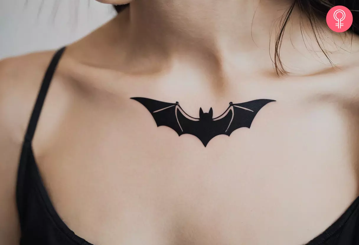 A minimalist flying bat tattoo on a woman’s chest 