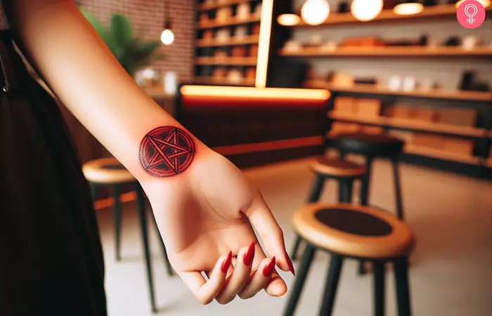 A red ink pentagram tattoo on the wrist of a woman