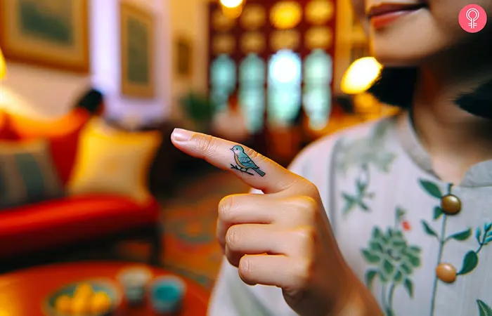 A small, minimalist bluebird tattoo on the finger of a woman