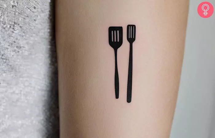 A minimalistic tattoo of a pair of spatula on the forearm