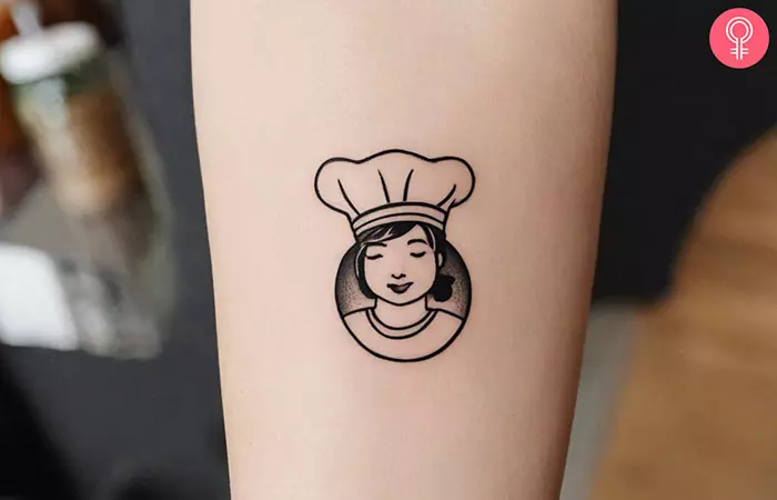 A tiny girl chef tattoo on the forearm