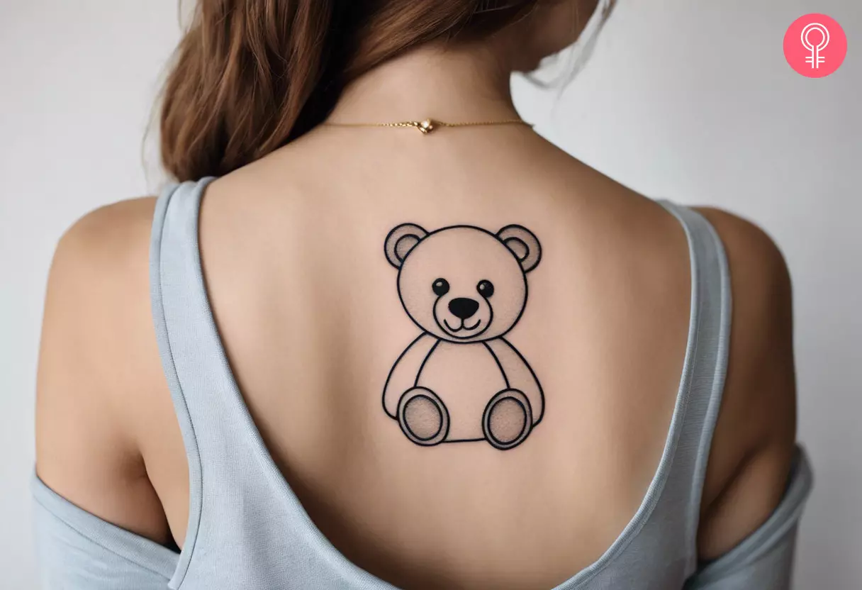 Woman with a fine line teddy bear tattoo on her upper back