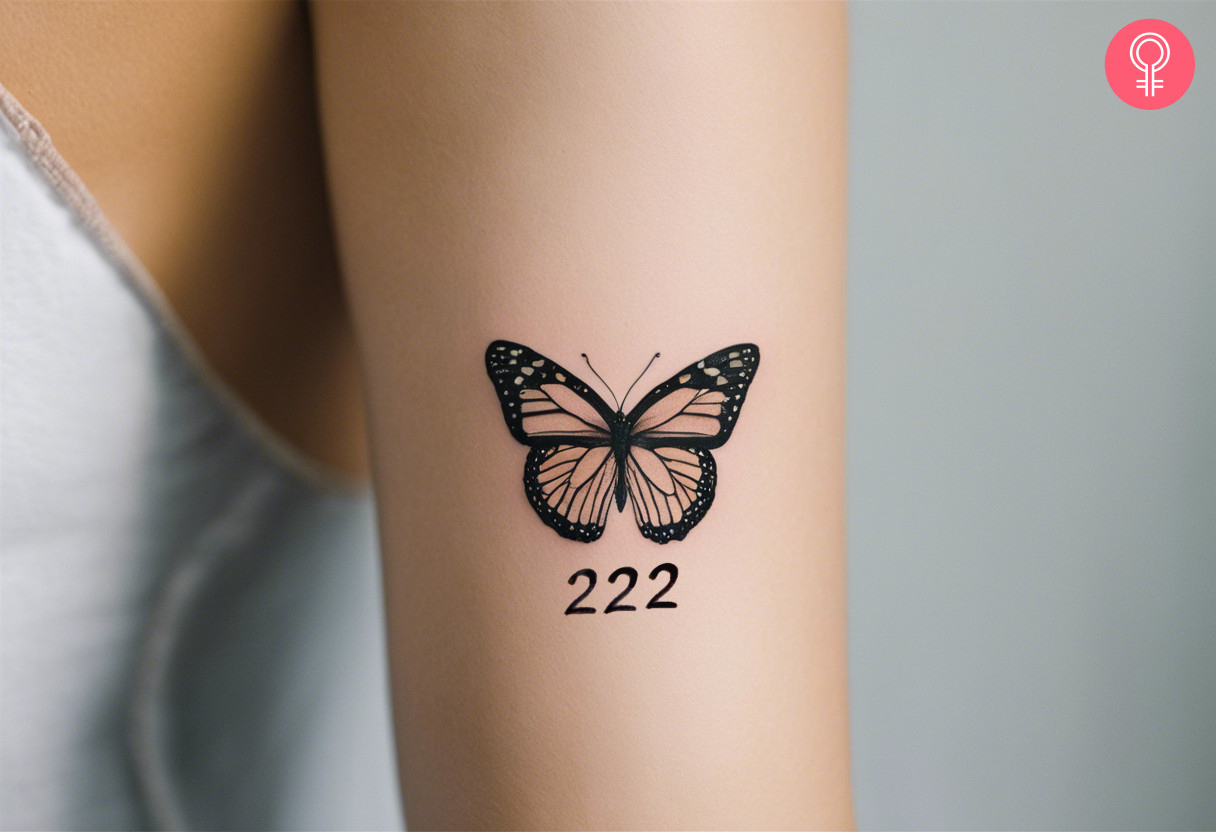 A 222 tattoo with a butterfly on a woman’s forearm