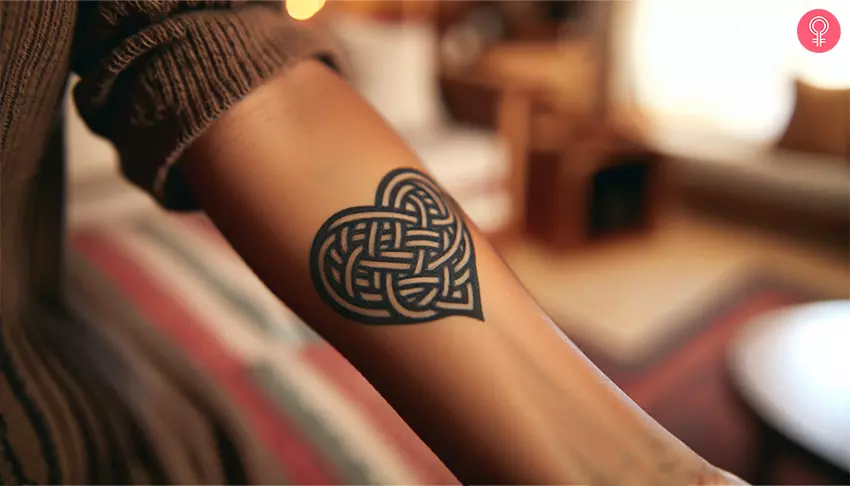 A Celtic knot heart tattoo on the wrist of a woman