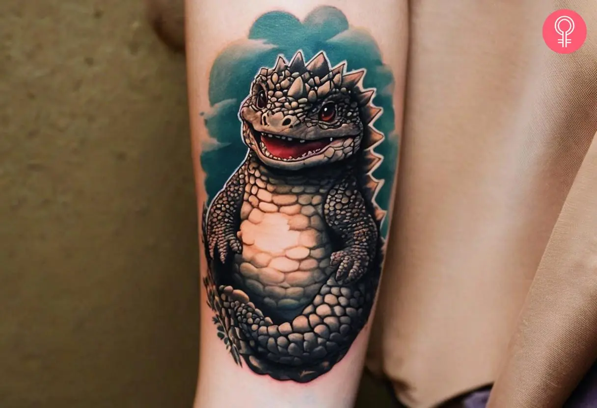 A baby Godzilla tattoo design on a woman’s forearm