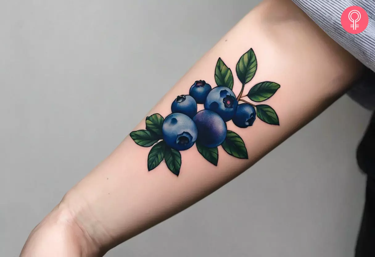 A blueberry bush tattoo on the forearm of a woman