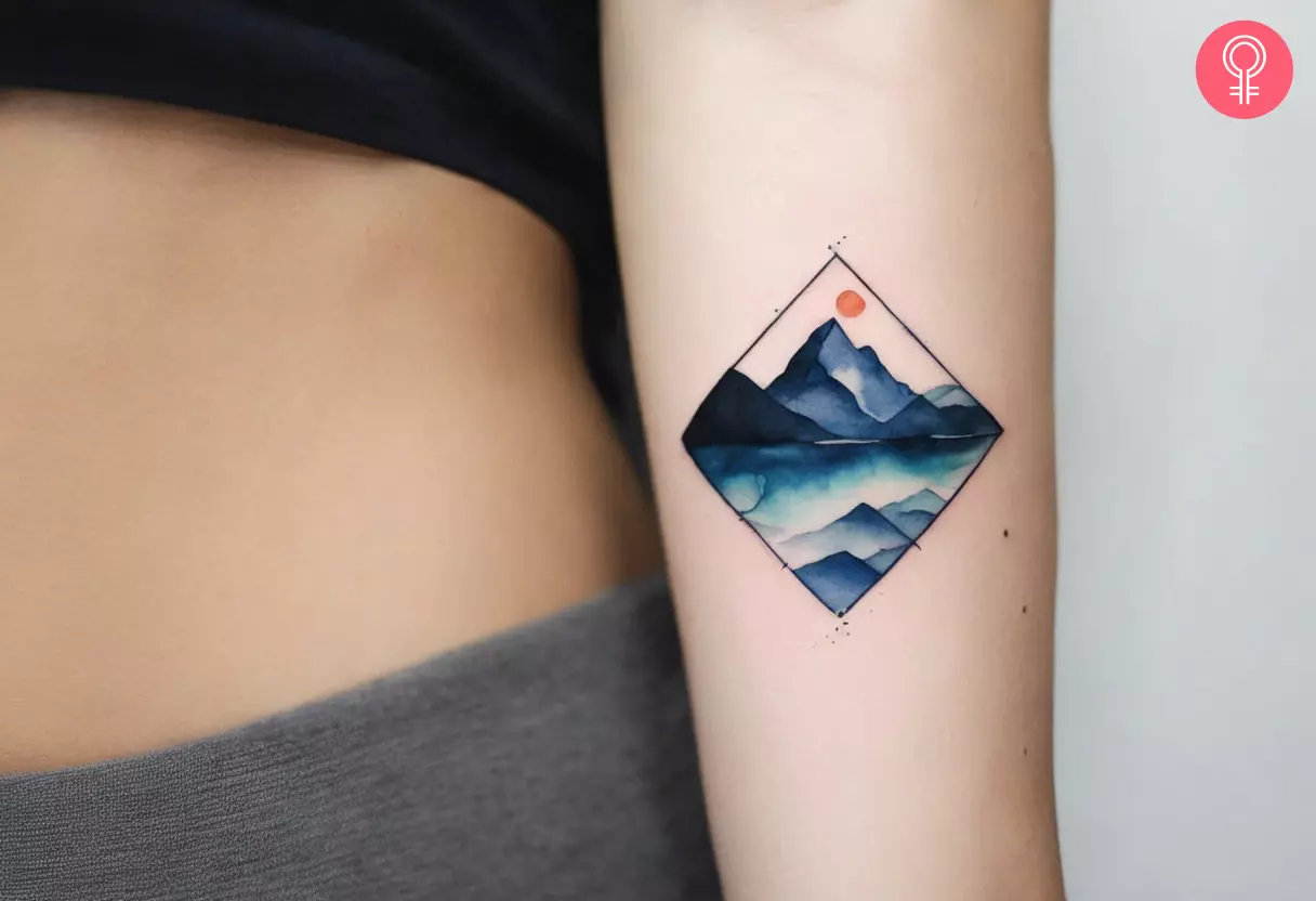 A dainty watercolor tattoo of a mountain on the upper arm
