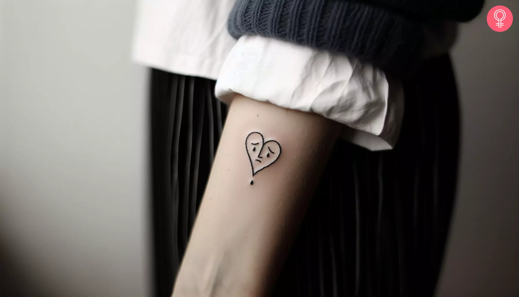 A heart with a sad face inked on the forearm