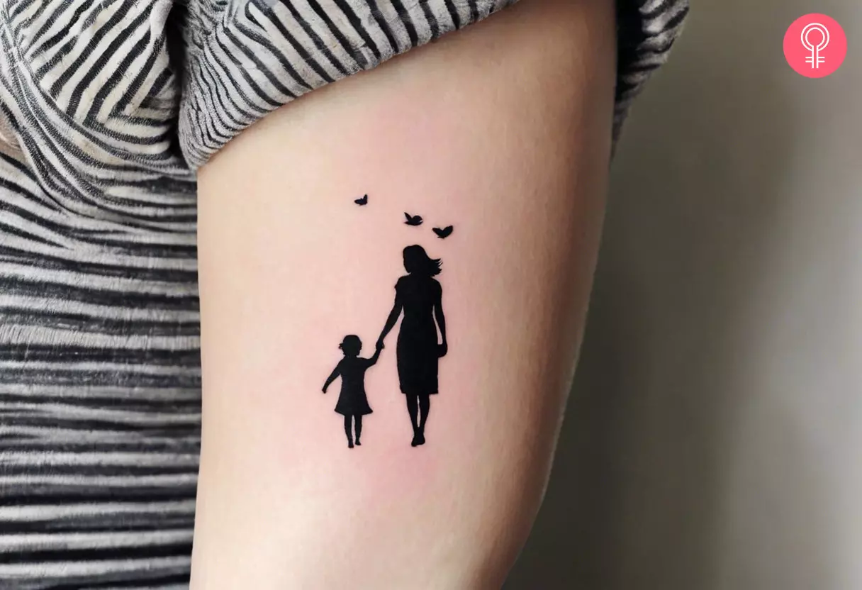 A silhouette tattoo of a mother and child inked on the upper arm