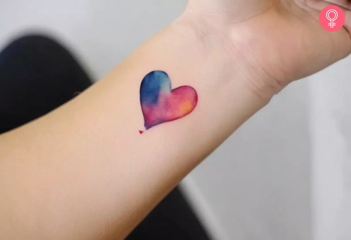 A woman wearing a watercolor heart tattoo on her inner wrist