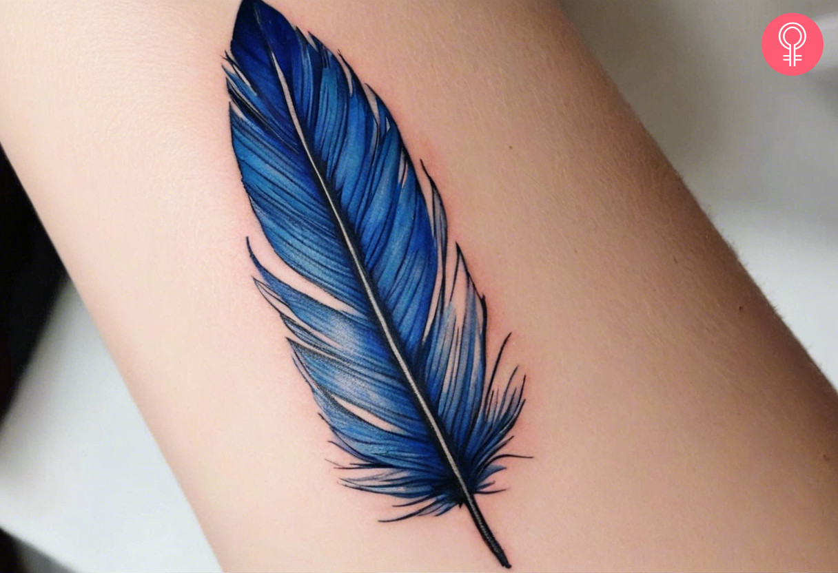 A close up of a blue jay feather tattoo on a woman’s forearm