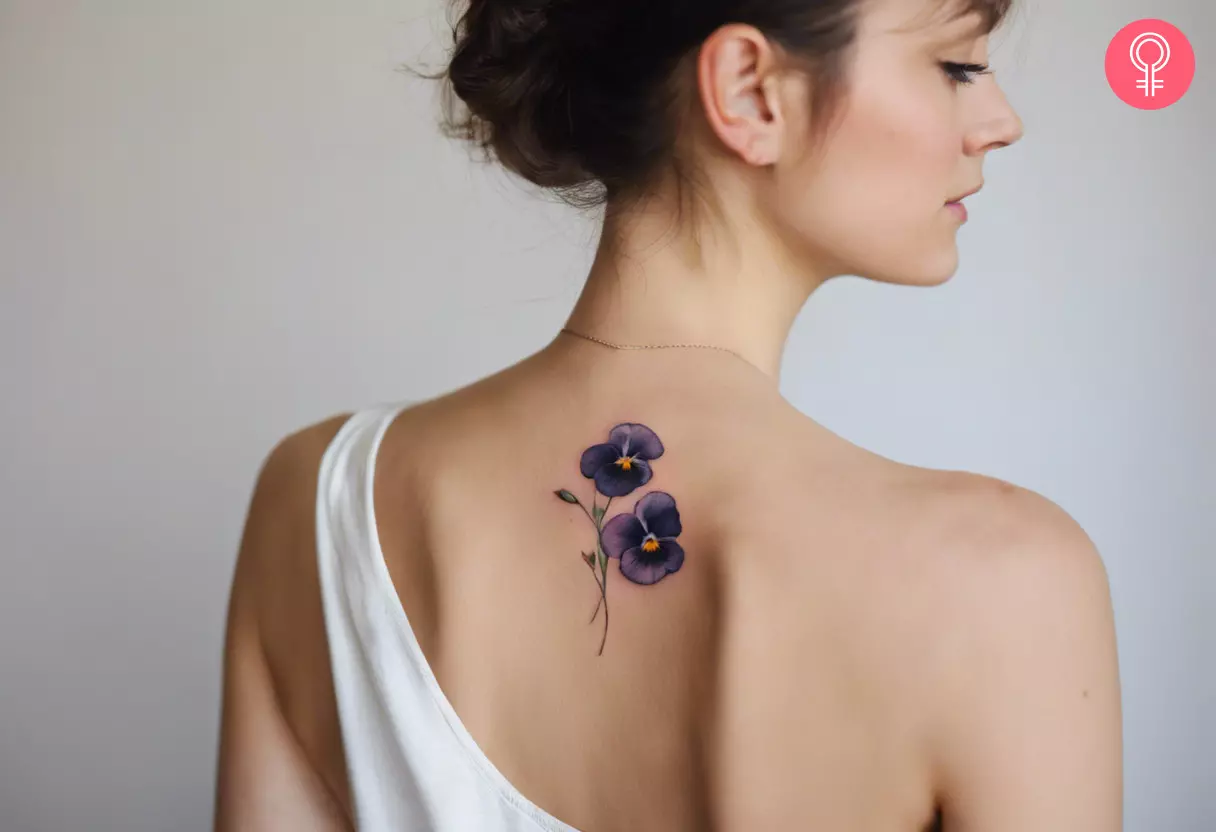 A delicate pansy tattoo on the upper back
