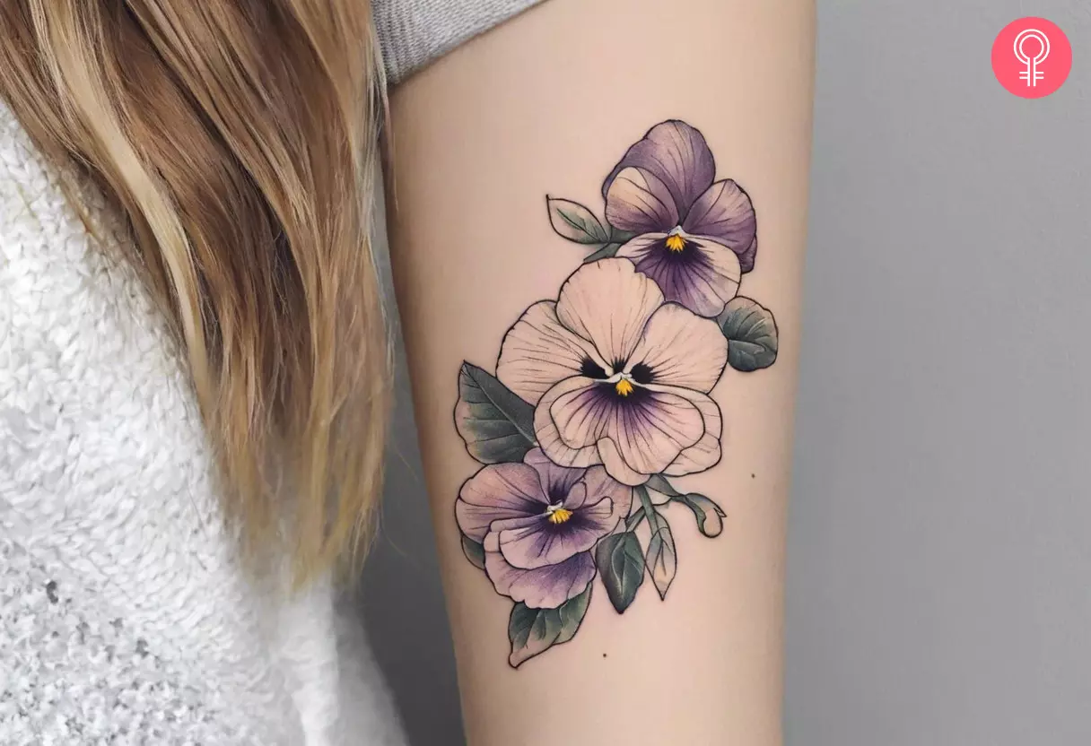 A fine line Pansy tattoo with subtle purple shading on the upper arm