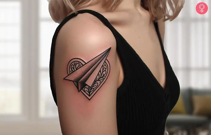 A heart paper airplane tattoo on a woman’s arm