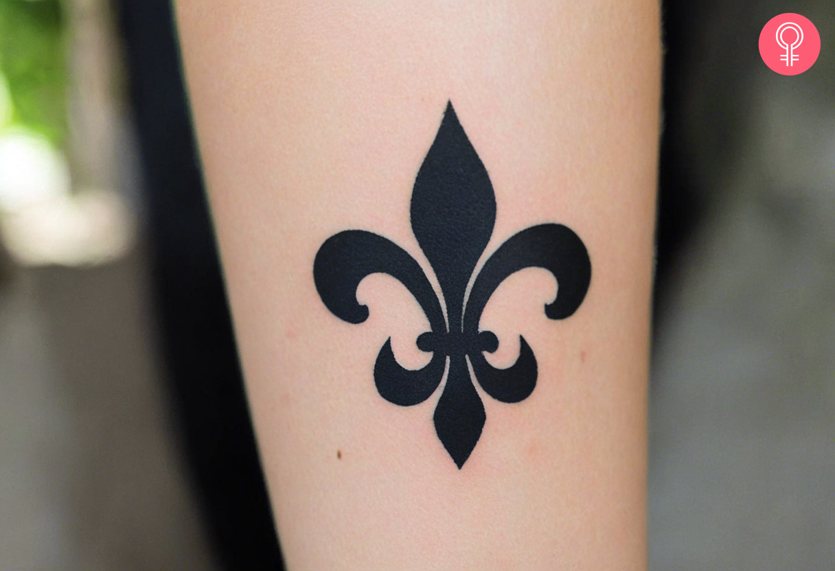 A minimalist fleur de lis tattoo on the forearm