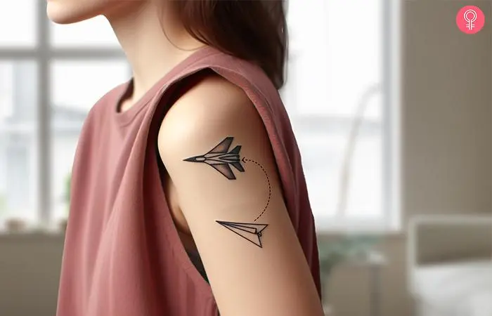 A paper airplane fighter jet tattoo on a woman’s upper arm