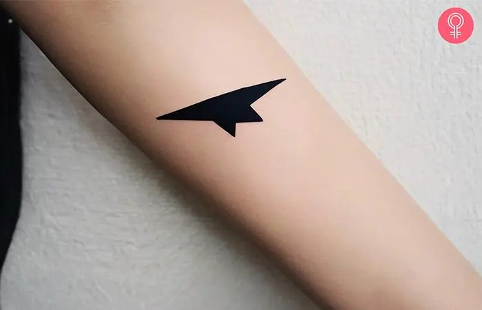 A paper airplane shadow tattoo on a woman’s forearm